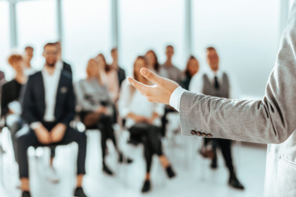 background image of a speaker standing in front of listeners in a conference room